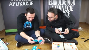 Dwóch dorosłych facetów siedzi i wypakowuje robociki Wonder Workshop